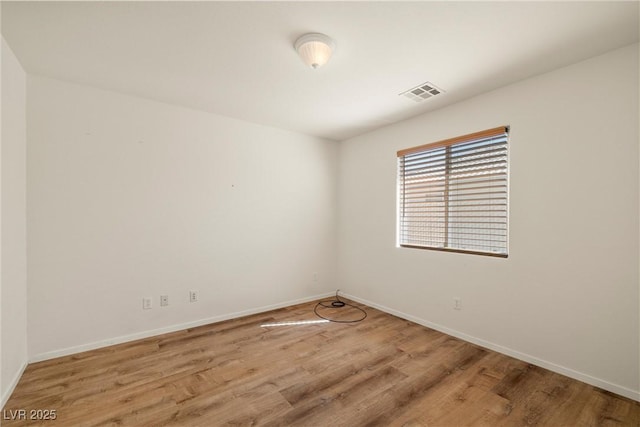 spare room with wood finished floors, visible vents, and baseboards