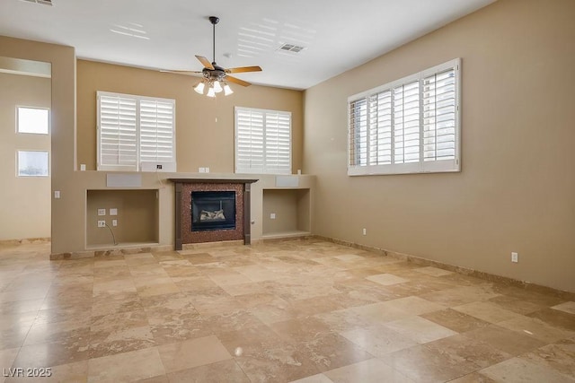 unfurnished living room with visible vents, baseboards, ceiling fan, and a tiled fireplace