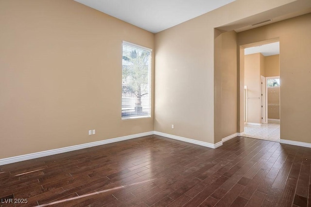 empty room featuring dark wood finished floors, visible vents, and baseboards