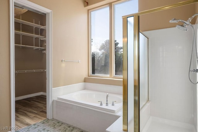 bathroom featuring a shower stall, a walk in closet, and a garden tub