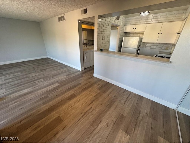 kitchen featuring freestanding refrigerator, dark wood-style flooring, visible vents, and a textured ceiling