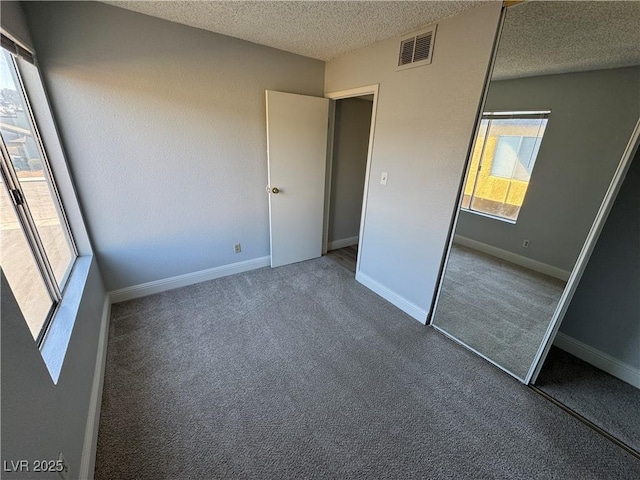 unfurnished bedroom featuring baseboards, visible vents, a textured ceiling, carpet flooring, and a closet