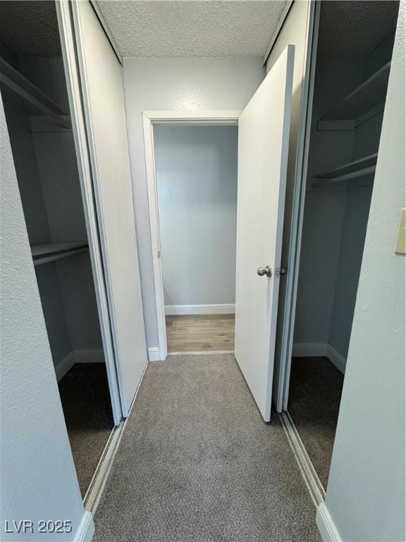 hall with a textured ceiling, carpet flooring, and baseboards