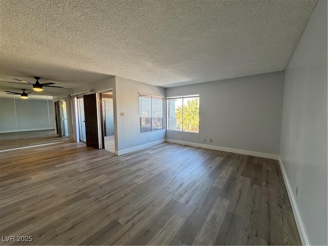 empty room with a textured ceiling, ceiling fan, wood finished floors, and baseboards