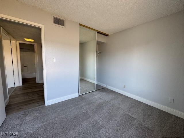 unfurnished bedroom featuring carpet, visible vents, a textured ceiling, and baseboards