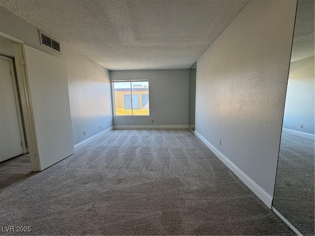 empty room with a textured ceiling, a textured wall, carpet floors, visible vents, and baseboards