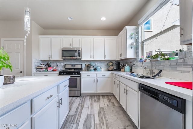 kitchen with stainless steel appliances, a sink, white cabinets, tasteful backsplash, and pendant lighting