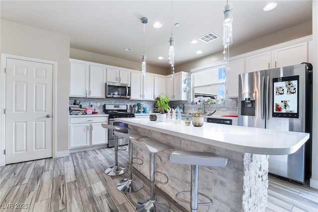 kitchen featuring decorative light fixtures, stainless steel appliances, light countertops, visible vents, and white cabinets