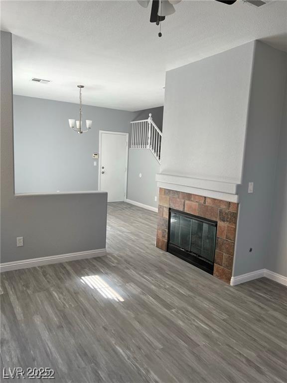 unfurnished living room with visible vents, baseboards, a glass covered fireplace, wood finished floors, and ceiling fan with notable chandelier