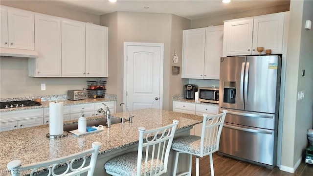 kitchen featuring stainless steel appliances, white cabinetry, under cabinet range hood, and a kitchen breakfast bar