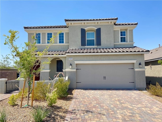 mediterranean / spanish-style house with decorative driveway, stucco siding, fence, a garage, and a tiled roof