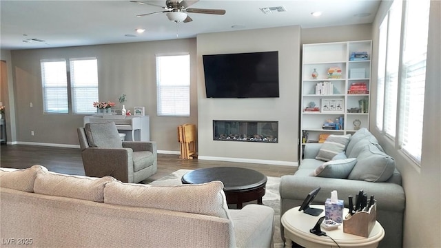 living area featuring wood finished floors, a glass covered fireplace, visible vents, and baseboards