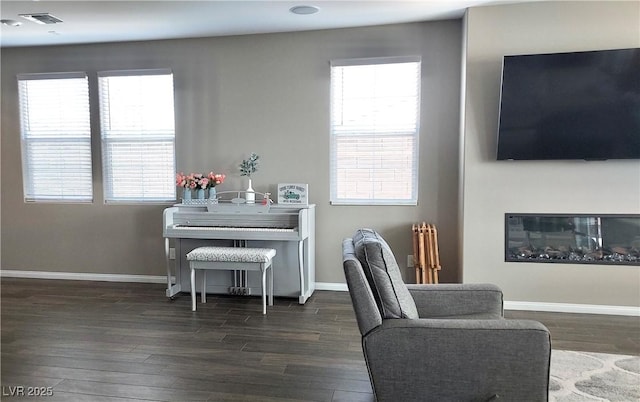 sitting room featuring a glass covered fireplace, wood finished floors, visible vents, and baseboards