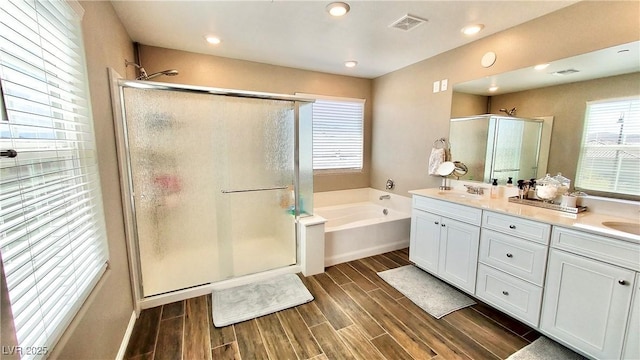 bathroom with double vanity, a stall shower, visible vents, wood finish floors, and a sink