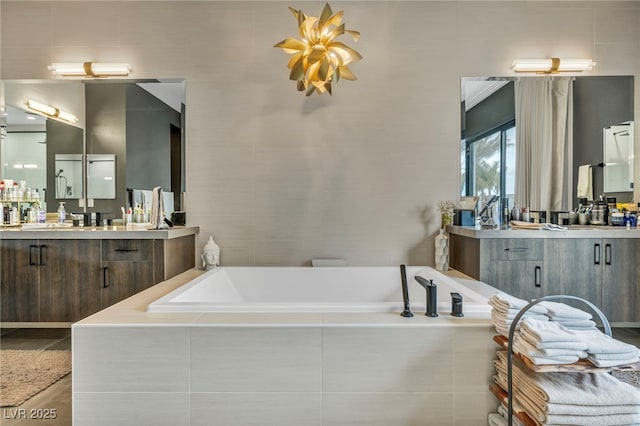 full bathroom with two vanities, a garden tub, and a sink