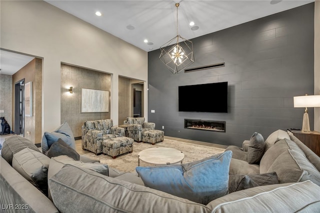 living room with recessed lighting, a high ceiling, an accent wall, a glass covered fireplace, and a chandelier