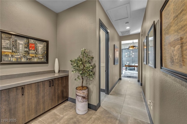 hall featuring a textured wall, visible vents, baseboards, and light tile patterned flooring