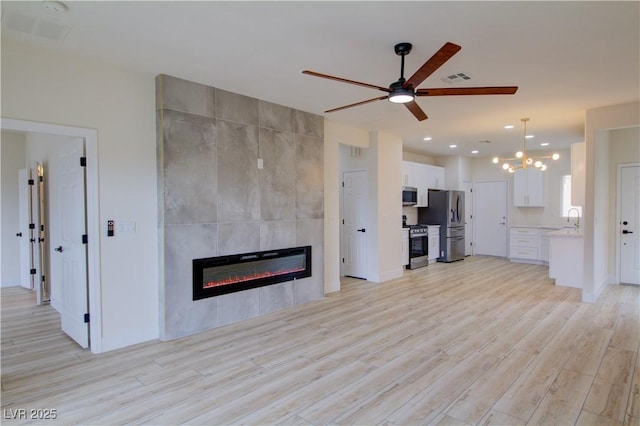 unfurnished living room featuring ceiling fan, a tile fireplace, a sink, visible vents, and light wood finished floors