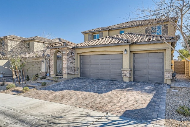 mediterranean / spanish-style house featuring a garage, a tile roof, stone siding, decorative driveway, and stucco siding