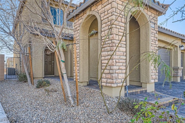 entrance to property with a garage, stone siding, a gate, and stucco siding