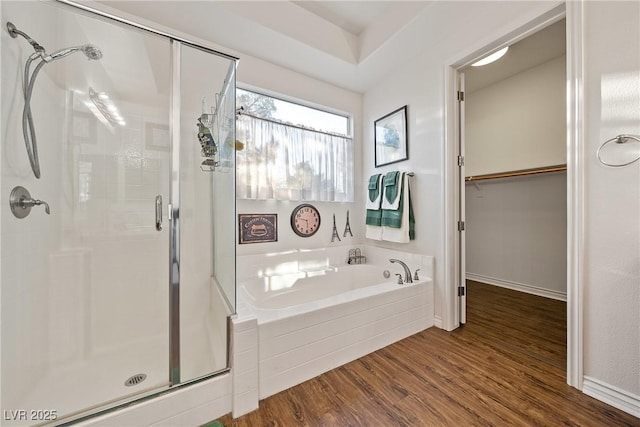 bathroom featuring a stall shower, wood finished floors, a bath, and a walk in closet