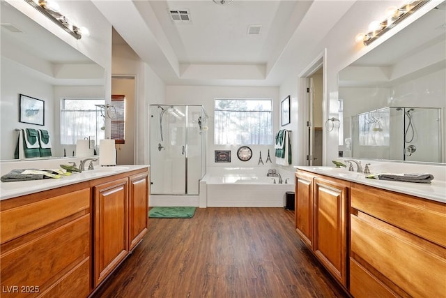 full bath with visible vents, a raised ceiling, wood finished floors, a shower stall, and a sink