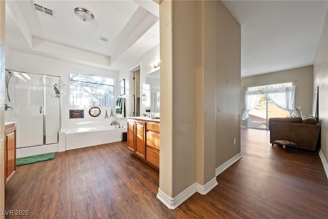 bathroom with a stall shower, a raised ceiling, a bath, and wood finished floors