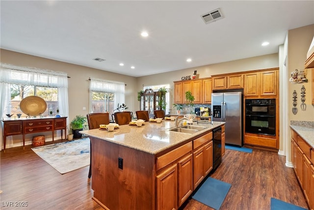 kitchen featuring a breakfast bar area, a sink, visible vents, black appliances, and dark wood finished floors