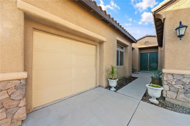 exterior space featuring an attached garage, stone siding, a tile roof, and stucco siding