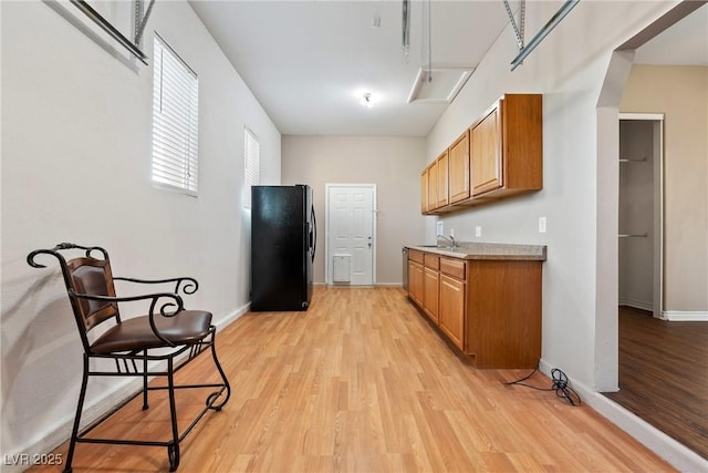 kitchen featuring a sink, light countertops, light wood-type flooring, freestanding refrigerator, and brown cabinetry