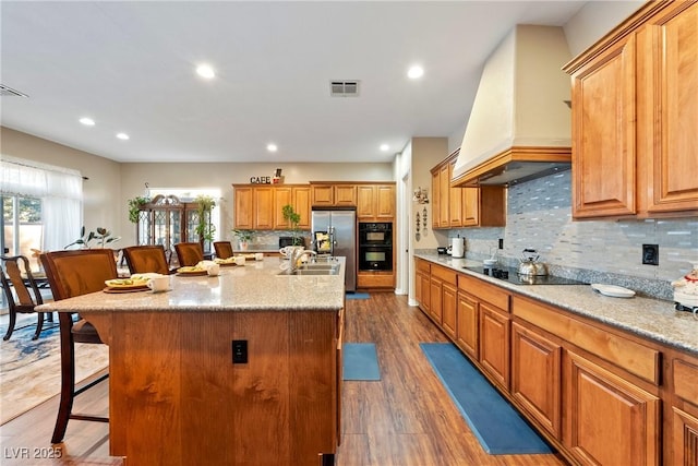 kitchen with visible vents, a breakfast bar area, black appliances, premium range hood, and a sink