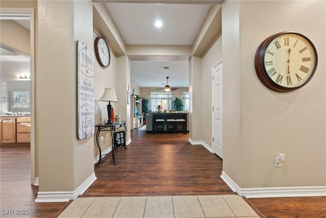 hall with wood finished floors, visible vents, and baseboards