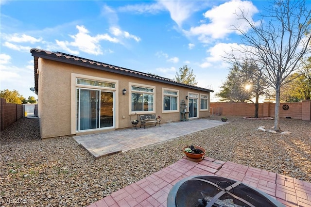 rear view of house with a patio, stucco siding, an outdoor fire pit, a fenced backyard, and a tiled roof