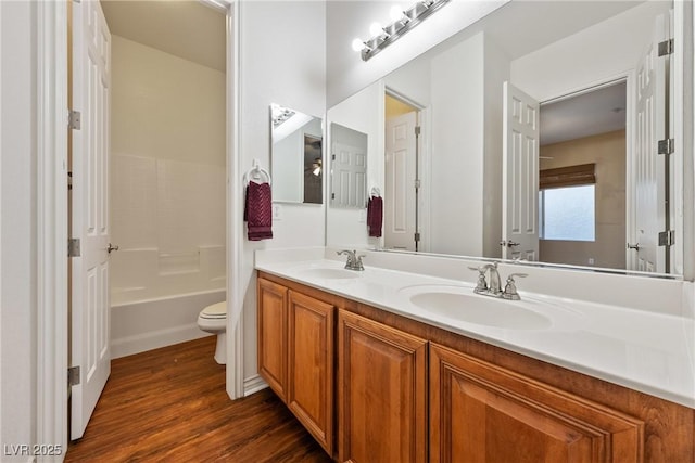 full bath with double vanity, a sink, toilet, and wood finished floors