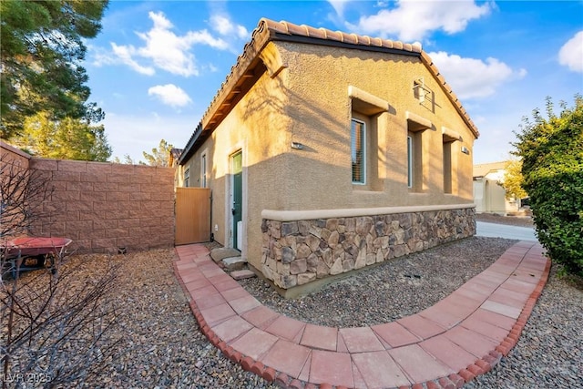 view of property exterior with stone siding, a tile roof, fence, and stucco siding