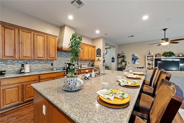 kitchen featuring a breakfast bar, tasteful backsplash, open floor plan, a kitchen island with sink, and light stone countertops