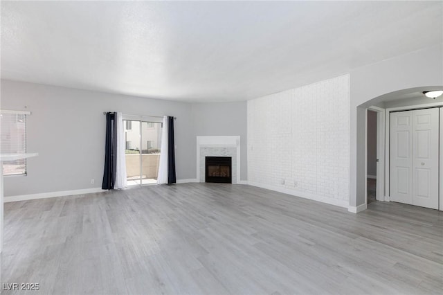 unfurnished living room featuring baseboards, a fireplace, arched walkways, and light wood-style floors