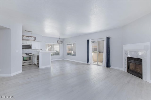 unfurnished living room with light wood finished floors, a tile fireplace, and baseboards