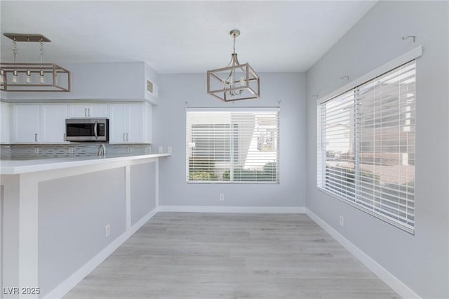 kitchen featuring white cabinetry, baseboards, hanging light fixtures, tasteful backsplash, and stainless steel microwave