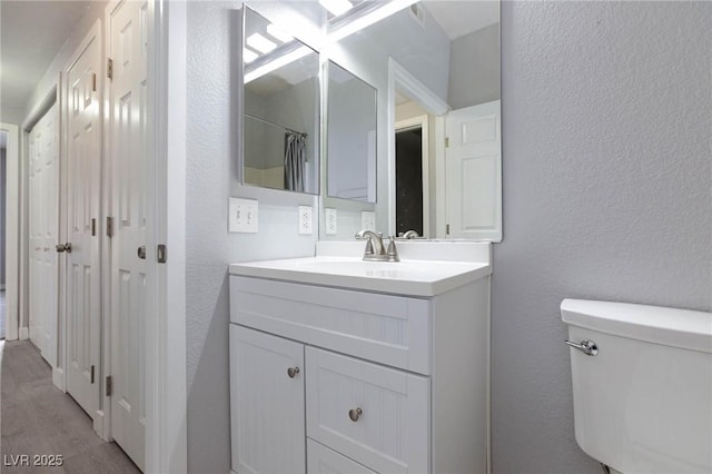 full bathroom featuring a textured wall, vanity, toilet, and wood finished floors