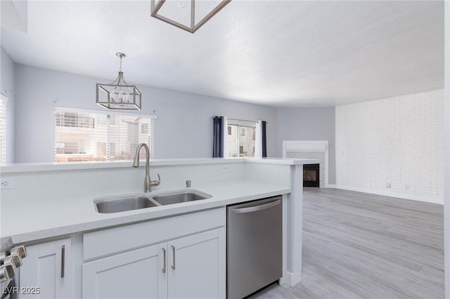 kitchen with dishwasher, light countertops, a fireplace, white cabinetry, and a sink