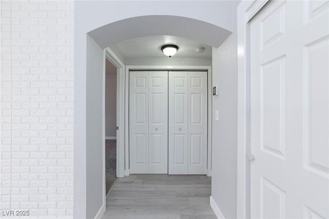 hall featuring light wood-style floors, arched walkways, brick wall, and baseboards