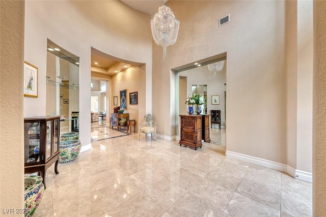 entrance foyer with a high ceiling, visible vents, a notable chandelier, and baseboards