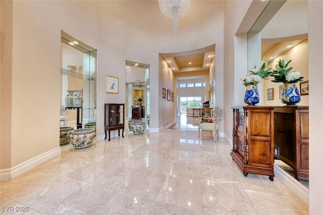 entryway featuring a tray ceiling, marble finish floor, a notable chandelier, a towering ceiling, and baseboards