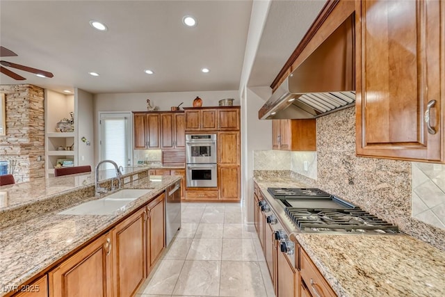 kitchen featuring ceiling fan, appliances with stainless steel finishes, light stone countertops, wall chimney range hood, and a sink