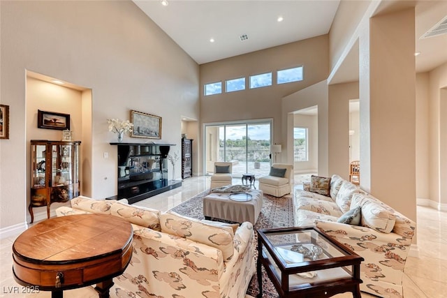 living room with a fireplace with raised hearth, a towering ceiling, visible vents, and baseboards