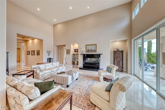 living room featuring marble finish floor, plenty of natural light, a towering ceiling, and a multi sided fireplace