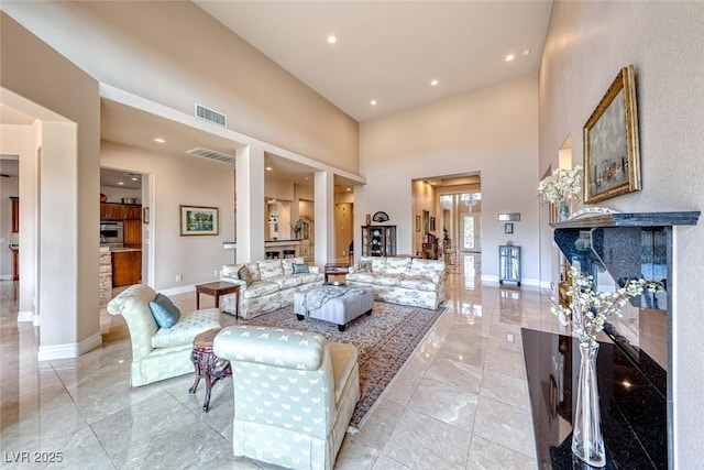 living area with baseboards, visible vents, a fireplace, and a high ceiling