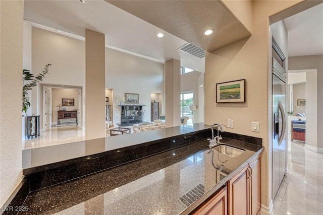 kitchen with a towering ceiling, dark stone countertops, stainless steel built in refrigerator, a sink, and recessed lighting