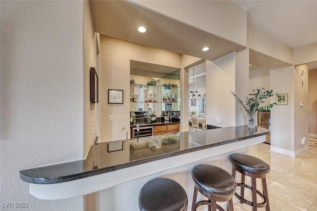 kitchen featuring a kitchen bar, recessed lighting, dark stone counters, beverage cooler, and baseboards